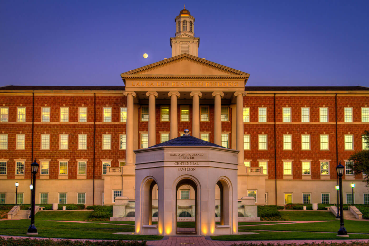 The Gail O. and R. Gerald Turner Centennial Pavilion sits proudly in front of the Laura Lee Blanton Building on the SMU campus with the moon rising in the background.