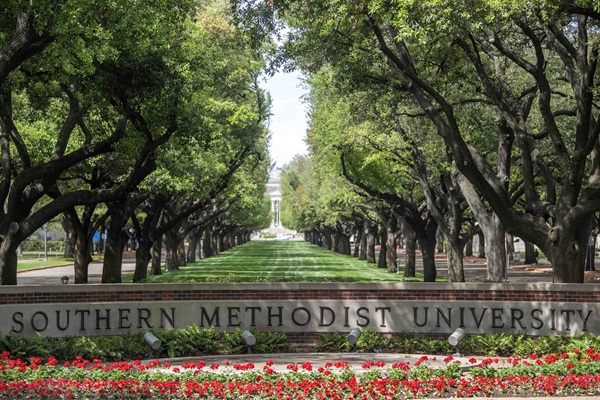 Oak lined entrance to Bishop Boulevard with a low brick sign spelling out Southern Methodist University