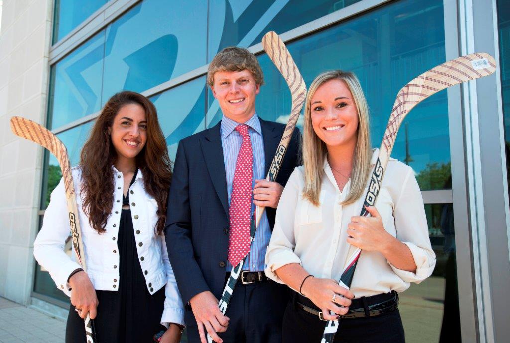 Three sports management graduate students holding hockey sticks.