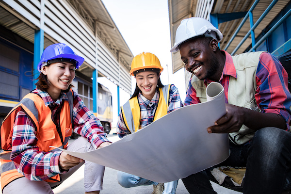 Two women and a man in hard hats looking at plans