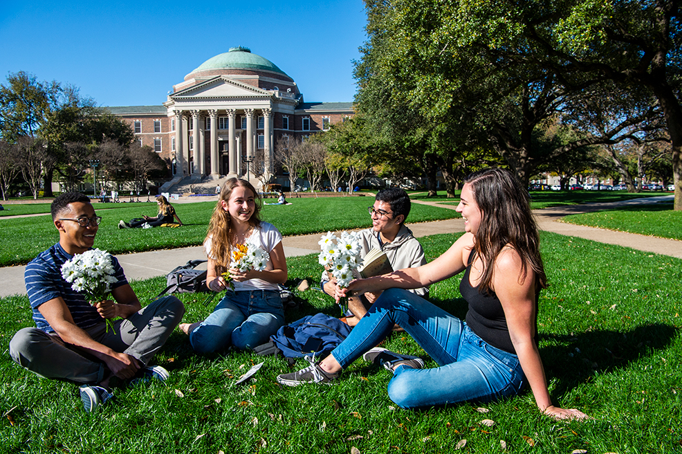 People holding flowers and sitting on the lawn of Dallas Hall