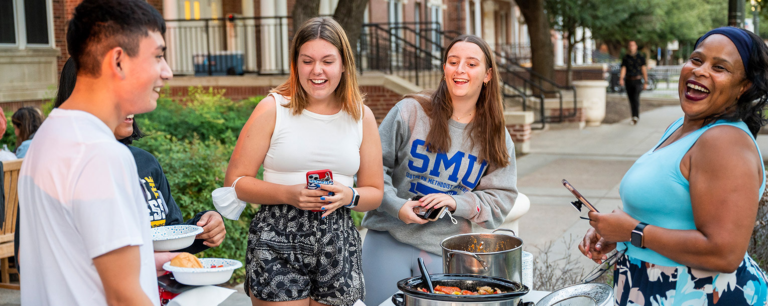 People gathered and laughing around a table while enjoying an outdoor meal.