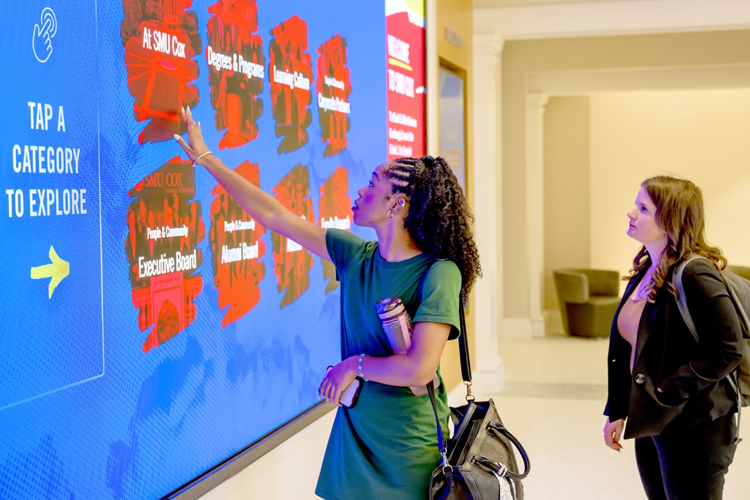 Student interacts with a wall touchscreen inside a Cox School building