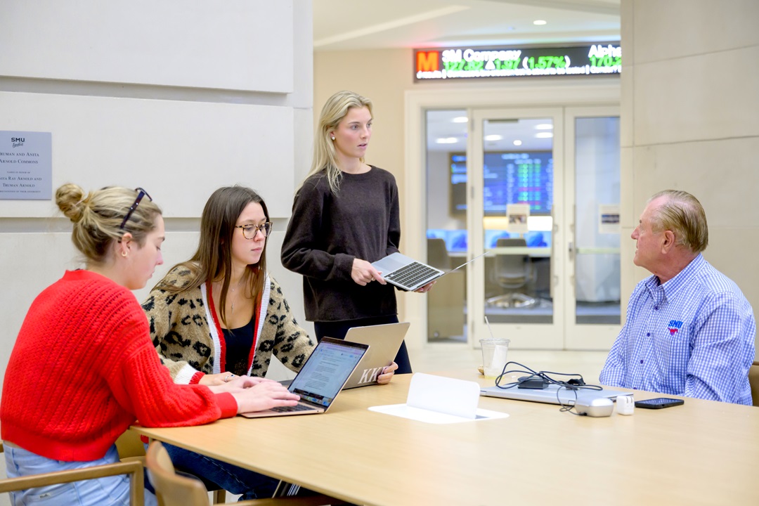 Students working on laptops talk to a faculty member
