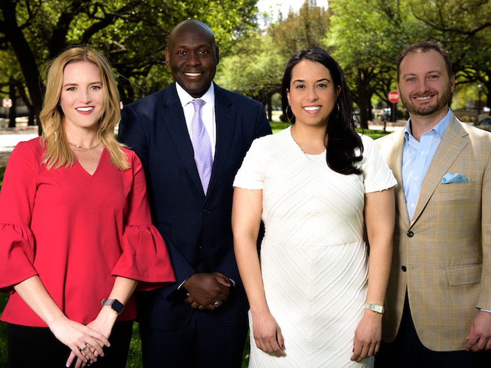 A group of four SMU Cox Online MBA students and faculty wearing professional clothing pose in front of trees outside