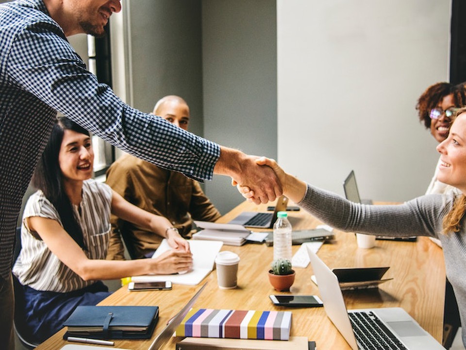 A group of MBA professionals sit at a table and two of the group members shake hands