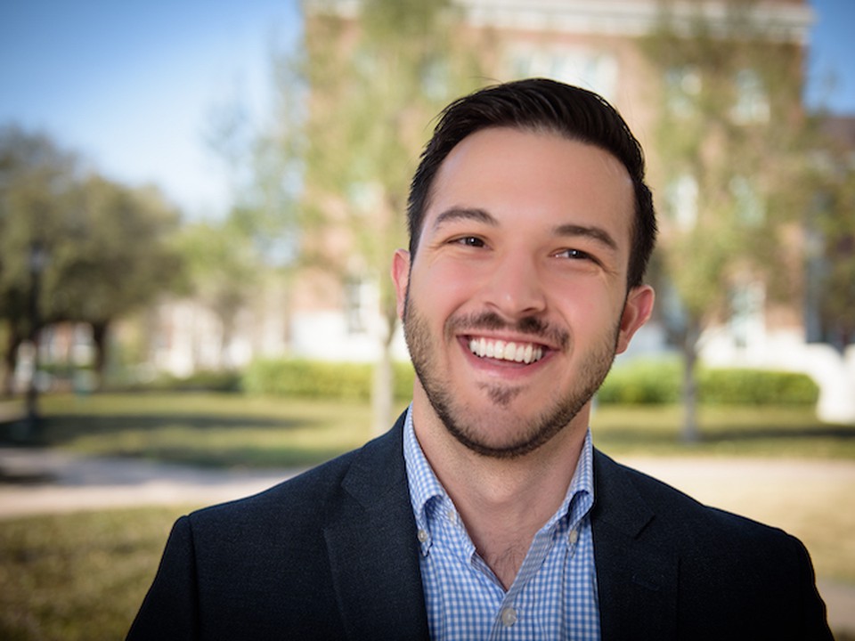 An SMU Cox MBA student wearing professional attire smiles while standing in front of a blurred outdoor scene