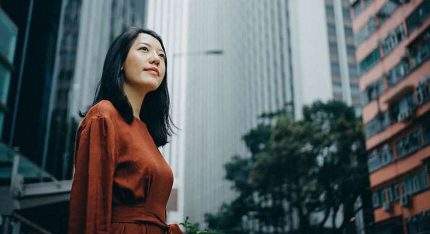 A female business administrator outside, in a city, looking up to the sky.