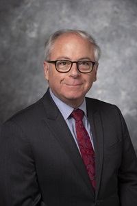 Dedman College Dean, Thomas DiPiero, smiles for a headshot in front of a gray background.