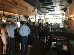 Dedman College alumni mingle at Izkina event in large room with wood panels, industrial lights, food, and a bar.