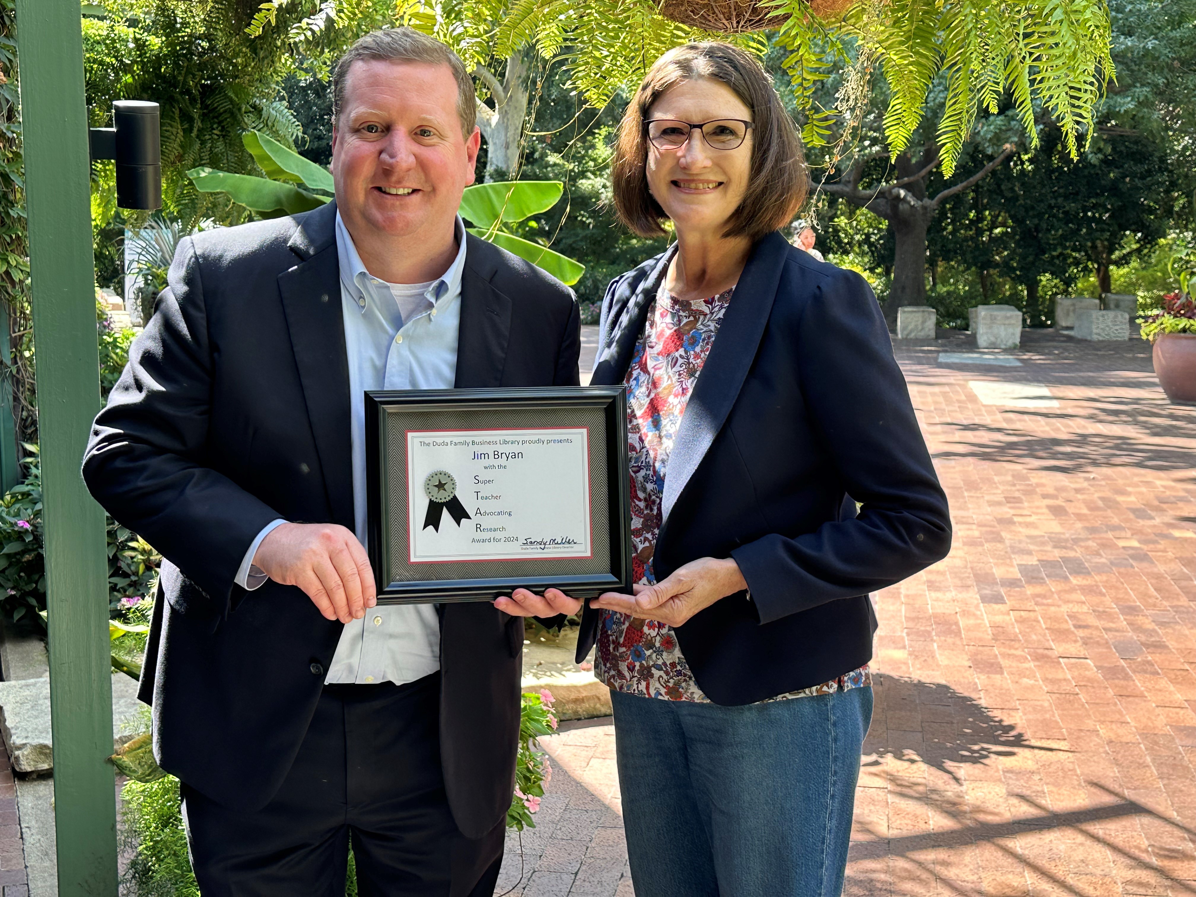 Jim Bryan, Associate Dean of BBA Undergraduate Program, holding the Duda Family Business Library's framed STAR Award with Sandy Miller, Director of the Duda Family Business Library