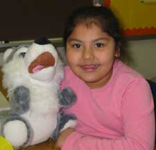 A girl sitting at a table with a stuffed animal, engrossed in an activity.