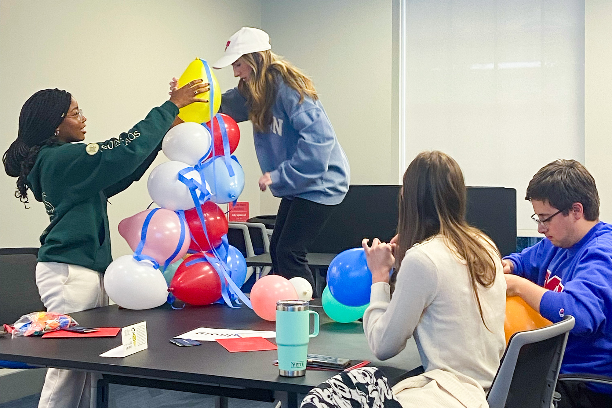 two students building tower with balloons and two students sitting at table inflating balloons