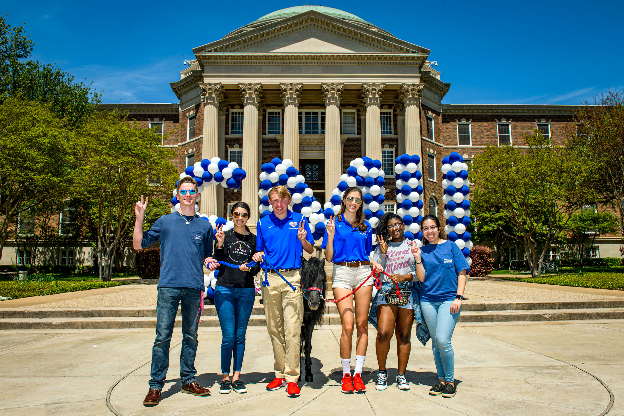 6 students posing in front of SMU signs in front of Dallas Hall