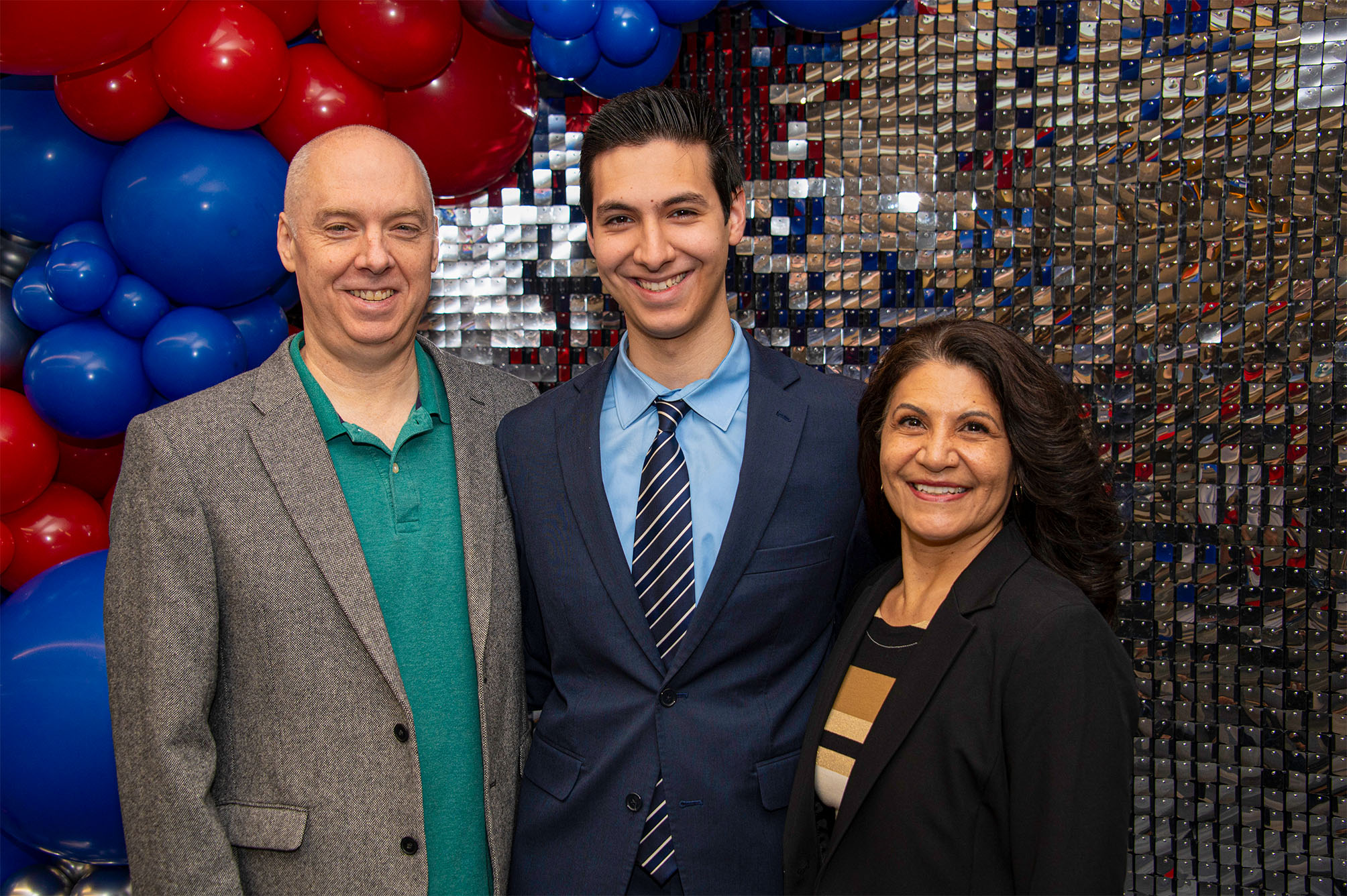 EJ Rorem and parents smiling and standing in front of silver sequined wall with red and blue balloons