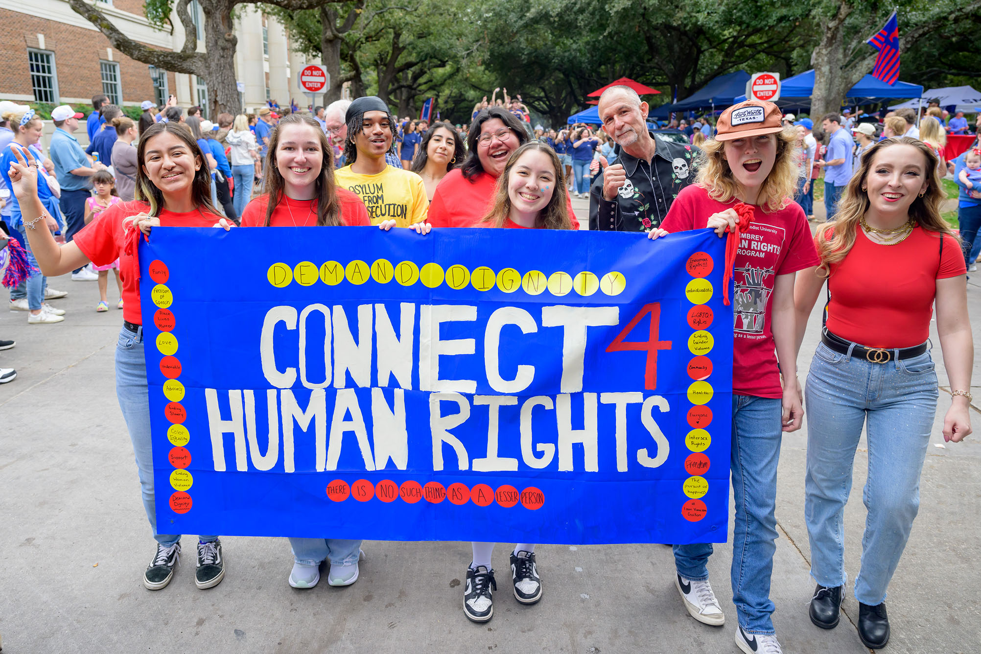 students in red shirts holding a blue banner outside that says Connect Human Rights in white with red and yellow dots